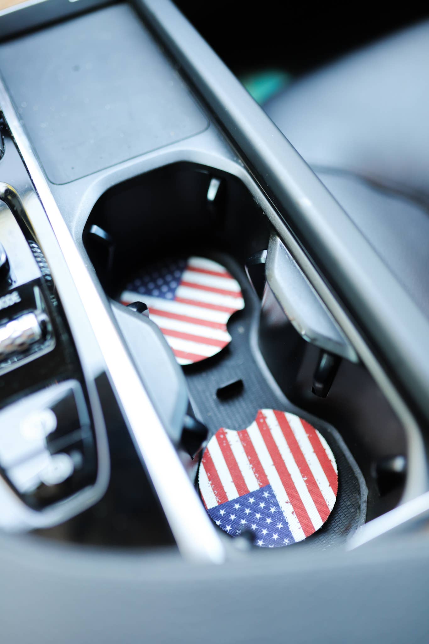 Two circular car cup holder coasters with a distressed American flag pattern, resting inside the cup holders of a car console.