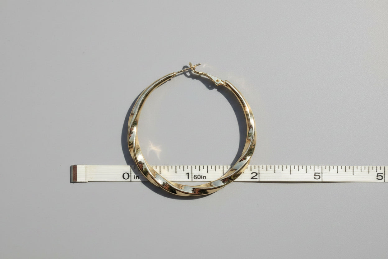Gold hoop earring on a ruler for size reference against a white background
