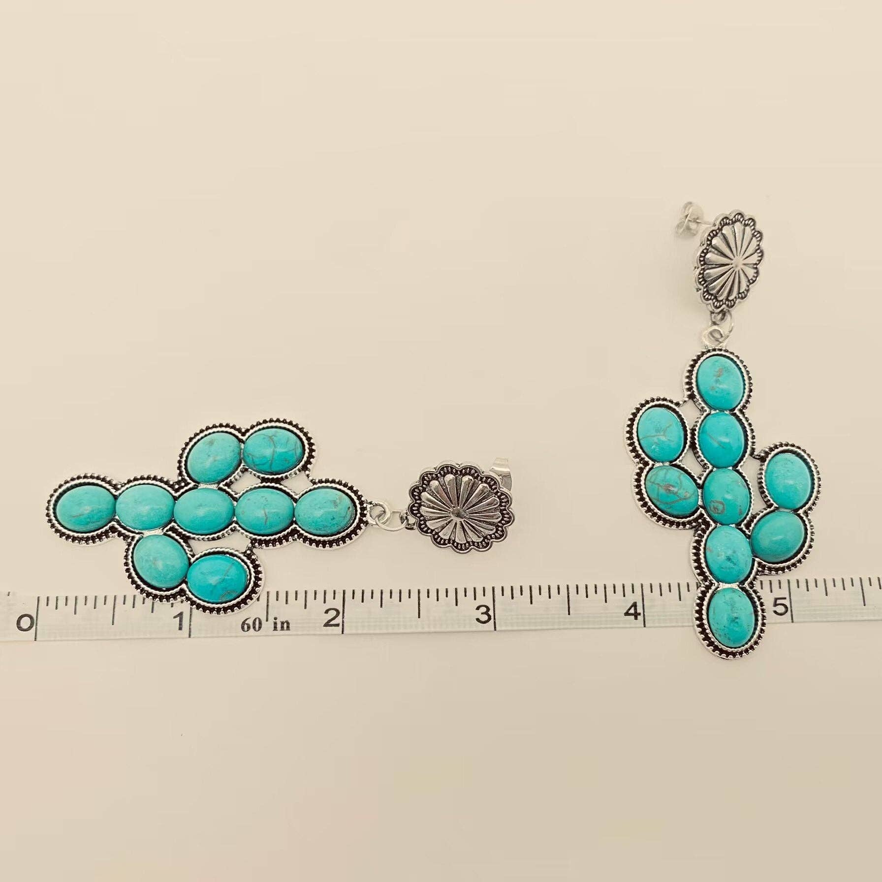 Turquoise earrings with silver accents on a beige background with a ruler for scale.