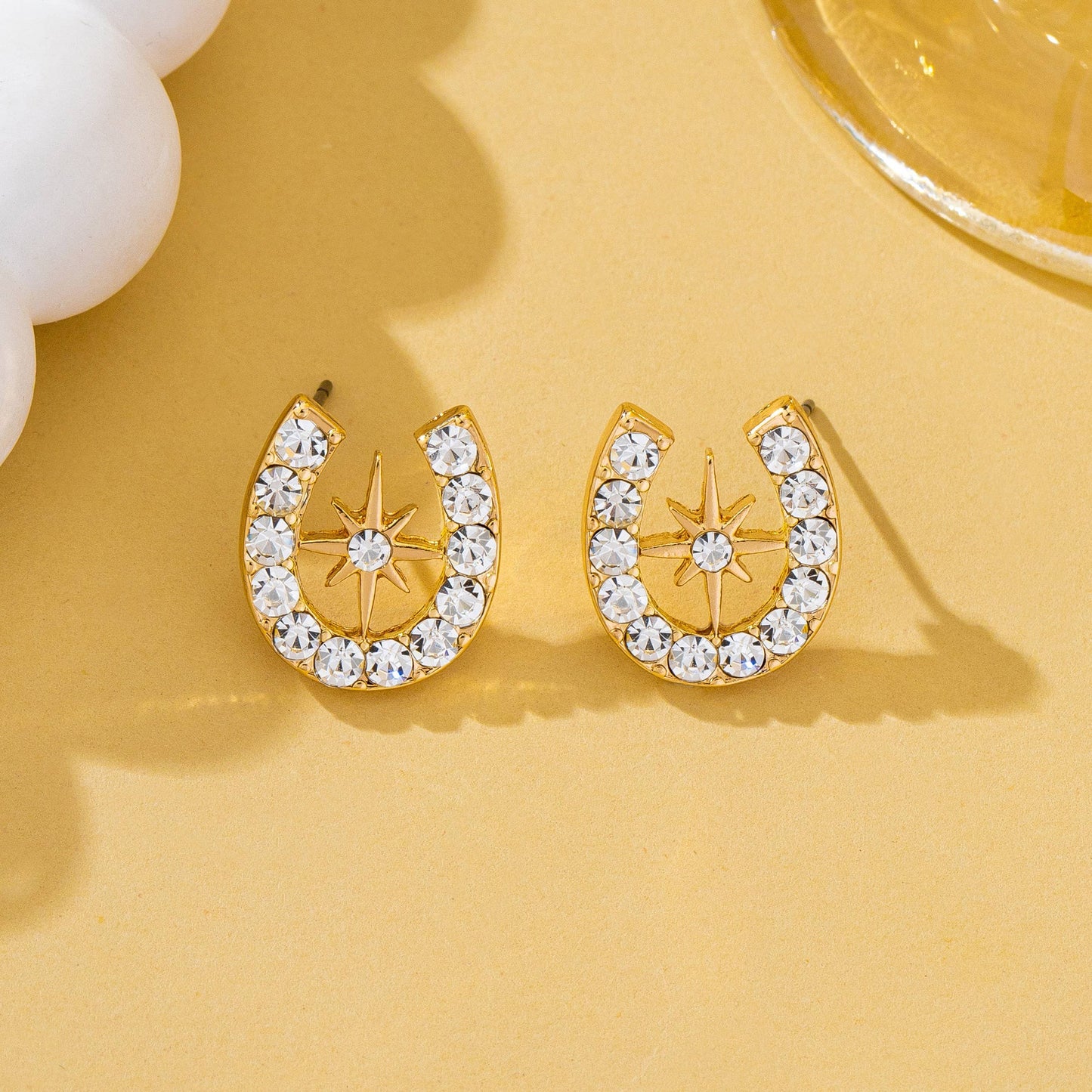 Gold horseshoe earrings with clear stones on a yellow background