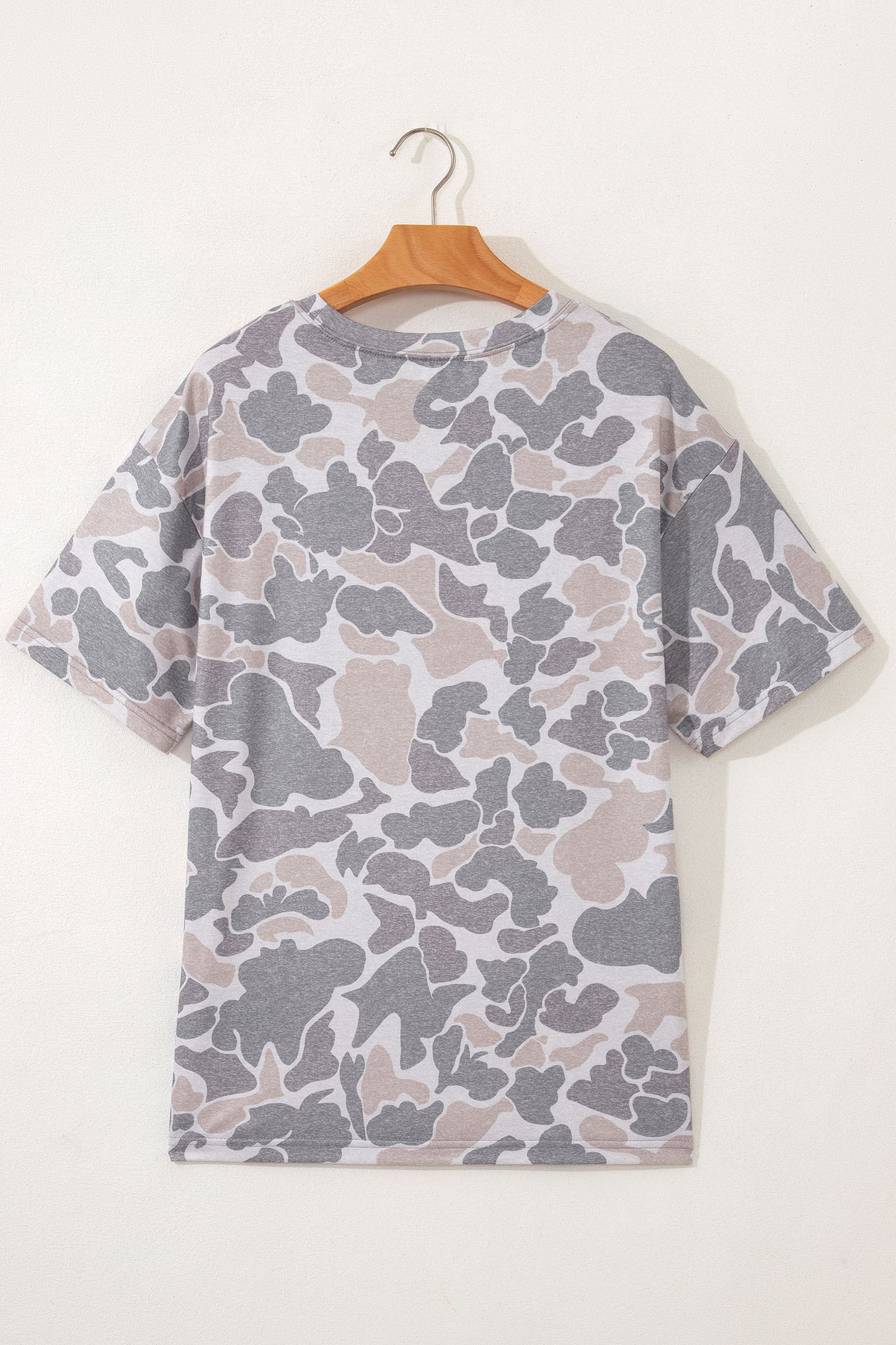 Camouflage-patterned t-shirt on a wooden hanger against a white background