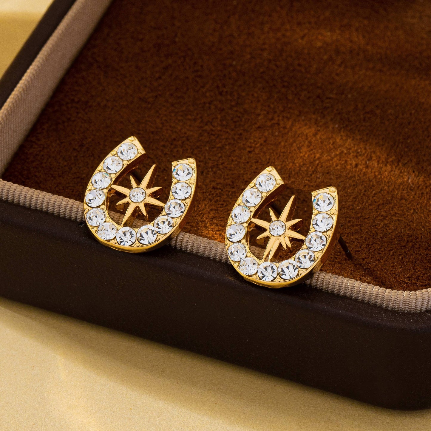Gold horseshoe earrings with star designs on a brown velvet surface