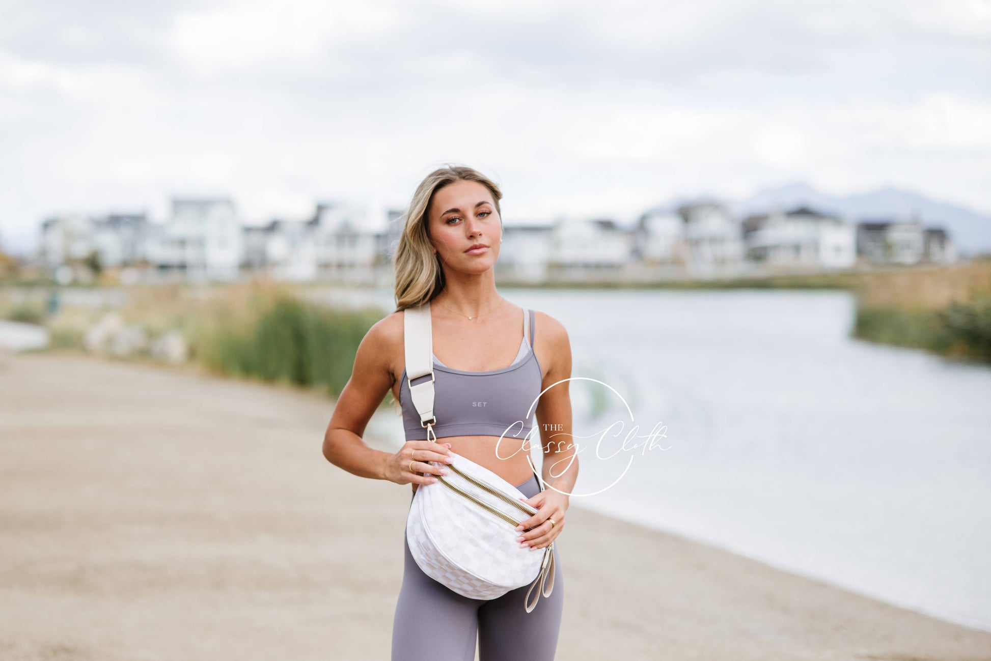 Woman in athletic wear standing by a waterfront with a white bag.