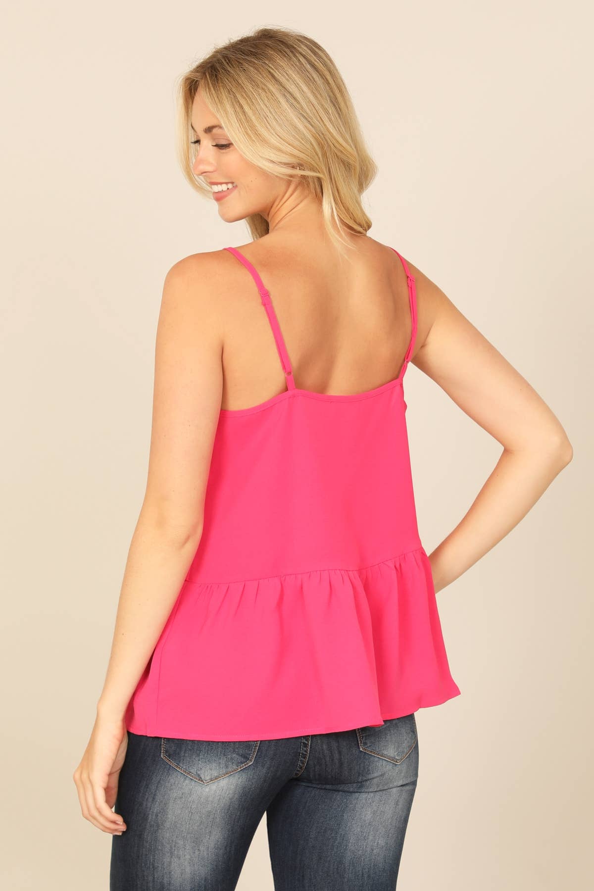 Woman wearing a bright pink tank top and blue jeans on a beige background
