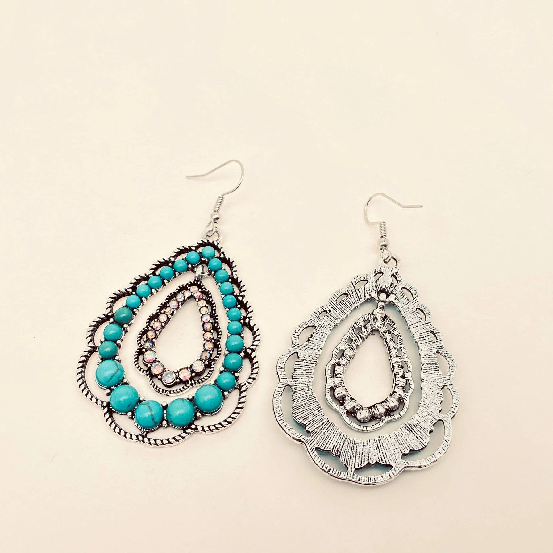 Pair of earrings with turquoise beads and silver designs on a beige background
