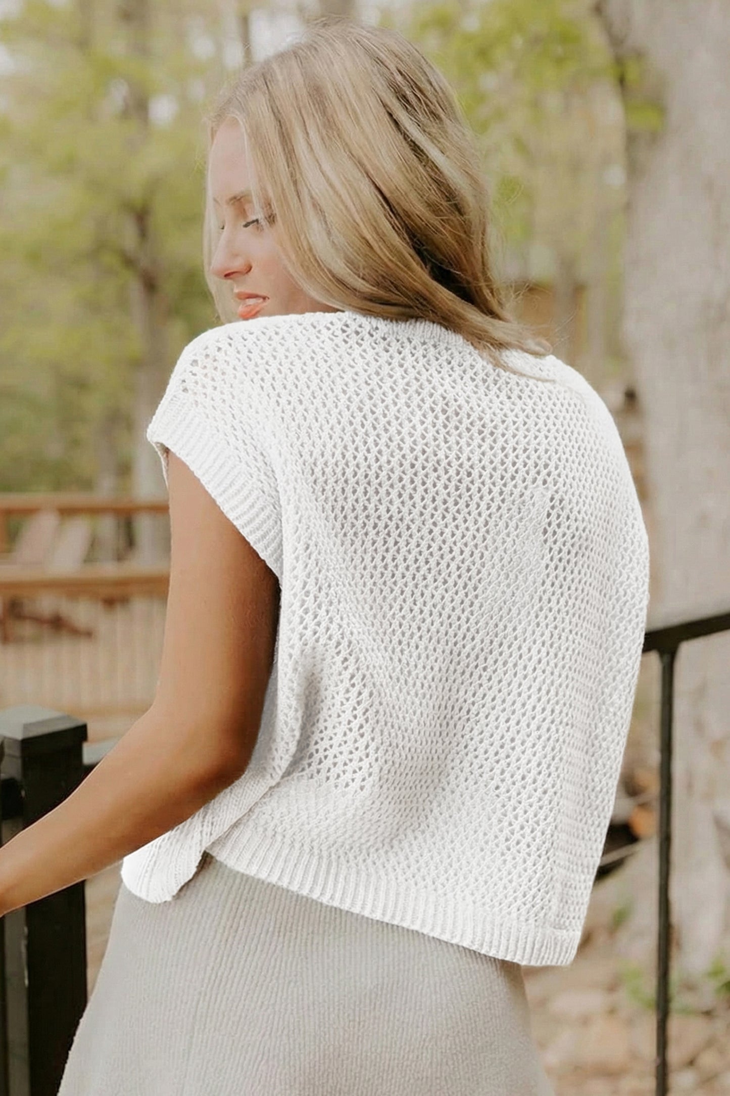 Woman wearing a white knitted top outdoors with trees in the background