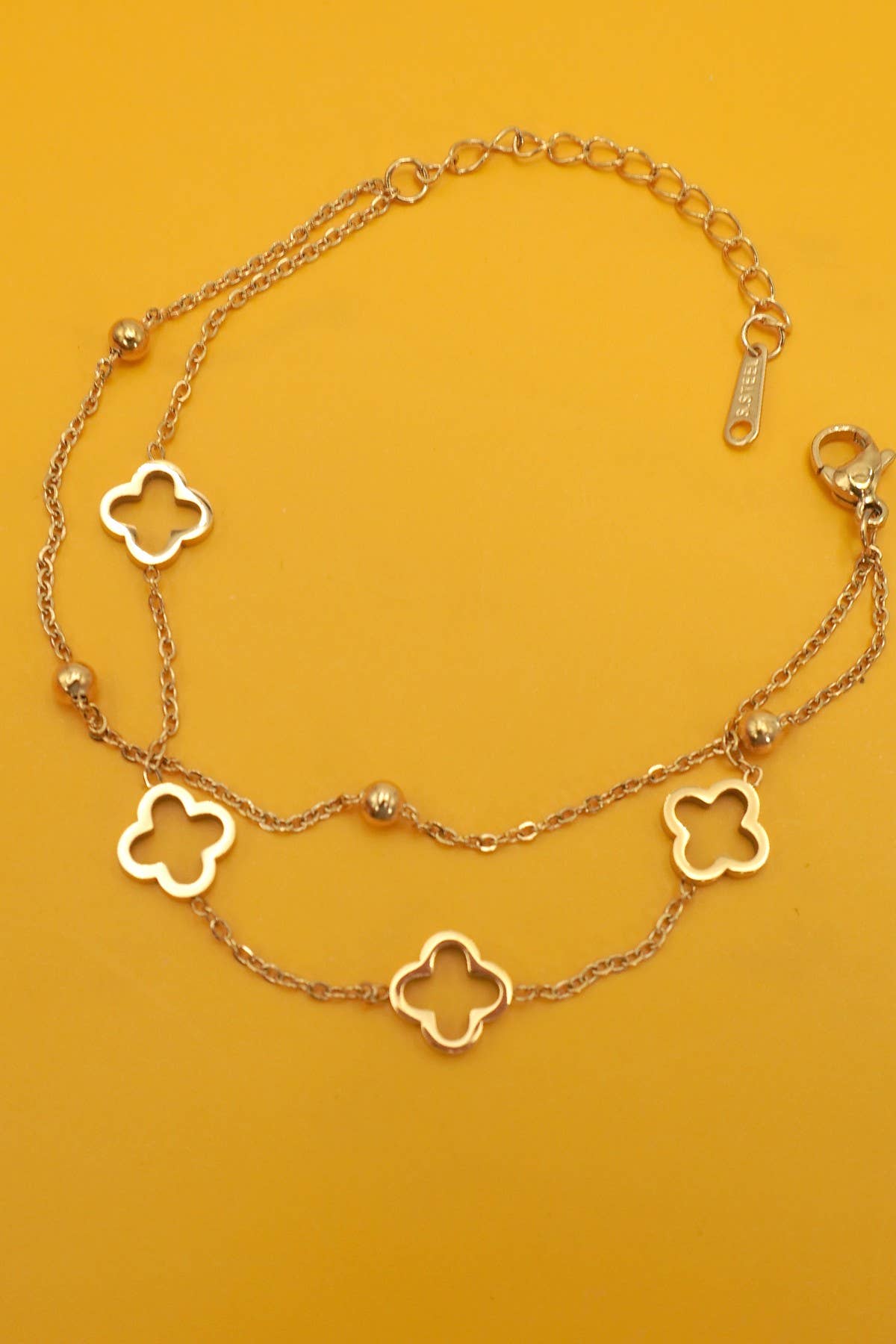 Gold bracelet with clover-shaped charms on a mustard yellow background
