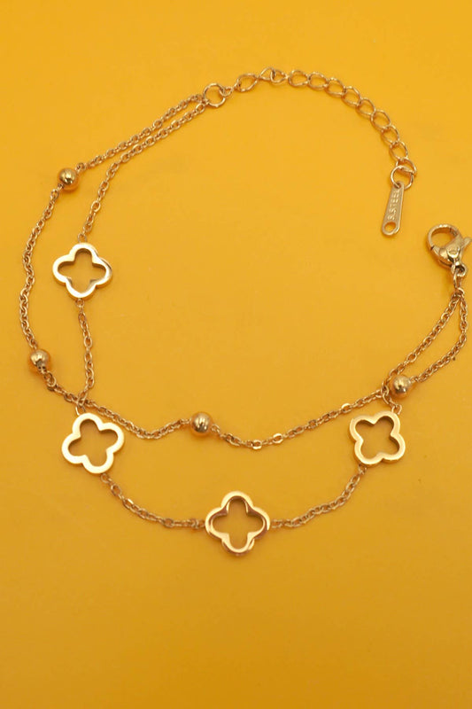 Gold bracelet with clover-shaped charms on a mustard yellow background