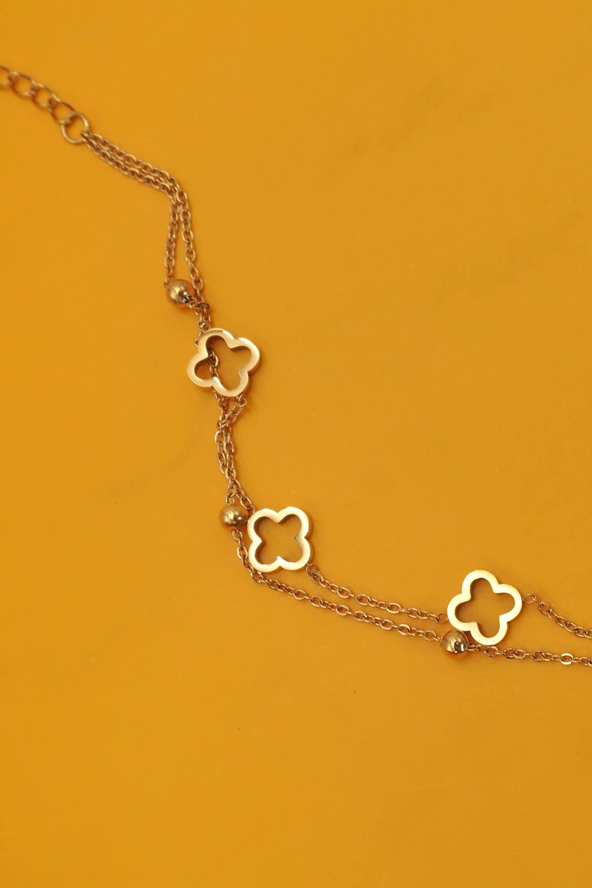 Gold necklace with clover-shaped pendants on a mustard yellow background
