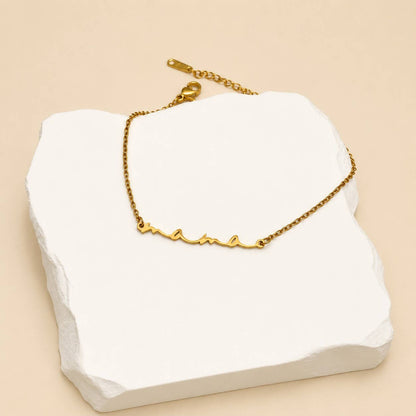 Dainty gold Mama script bracelet displayed on a white jewelry stand
