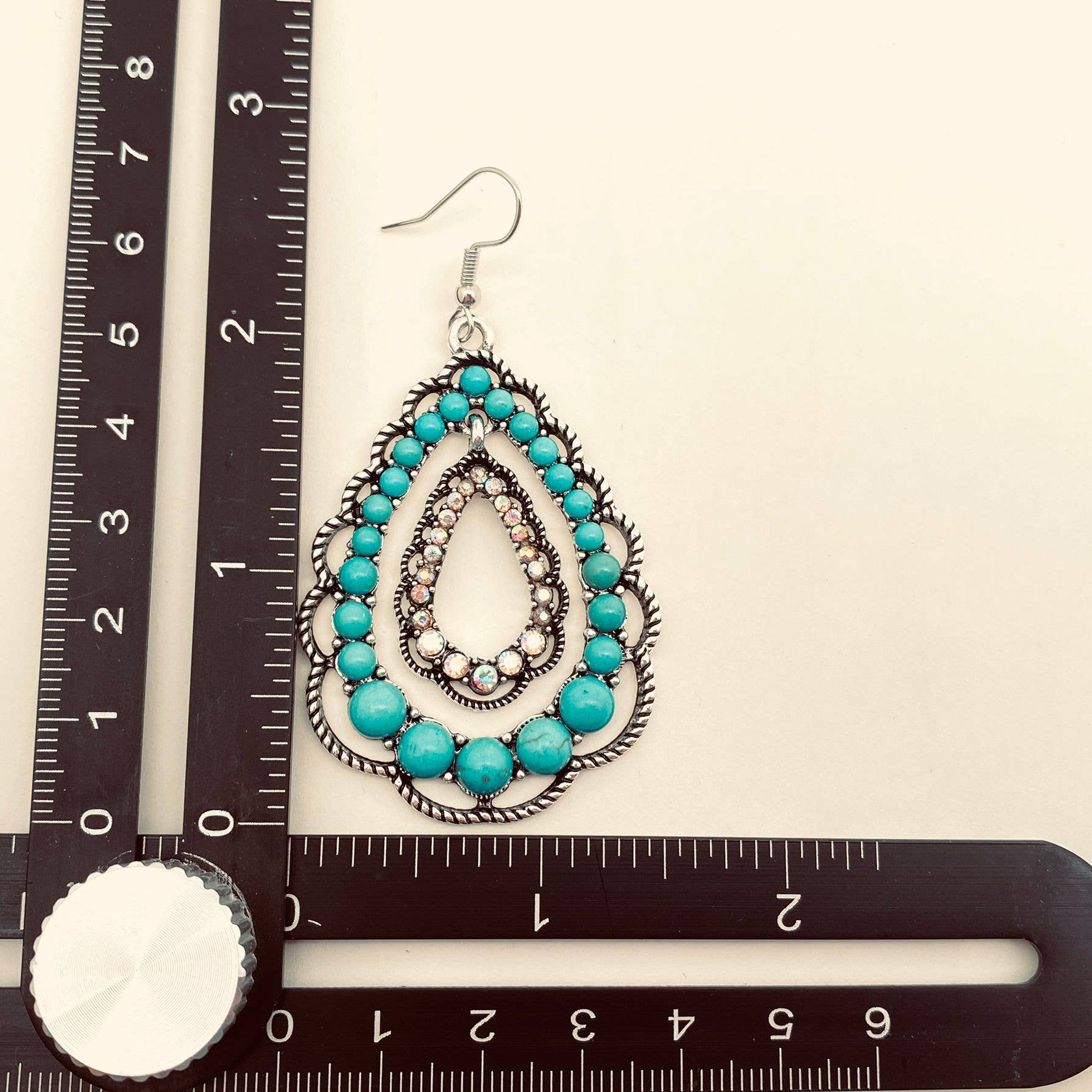 Teal beaded earring on a ruler for scale