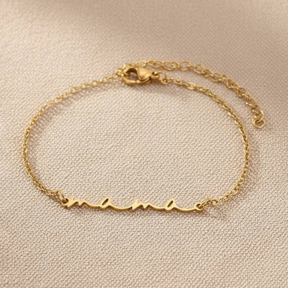 Gold PVD stainless steel Mama script bracelet displayed on neutral fabric
