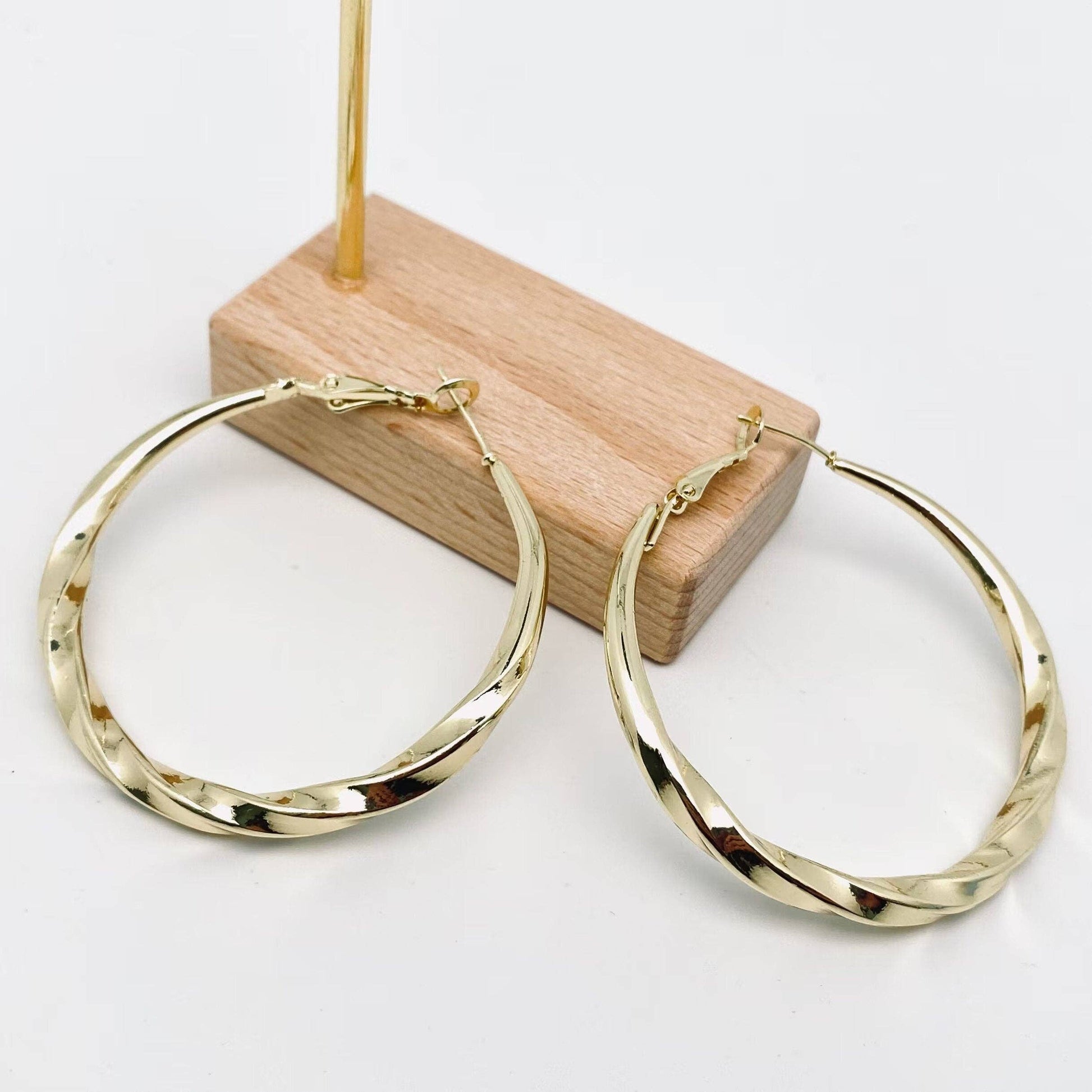 Gold hoop earrings on a wooden stand with a white background