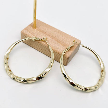 Gold hoop earrings on a wooden stand with a white background