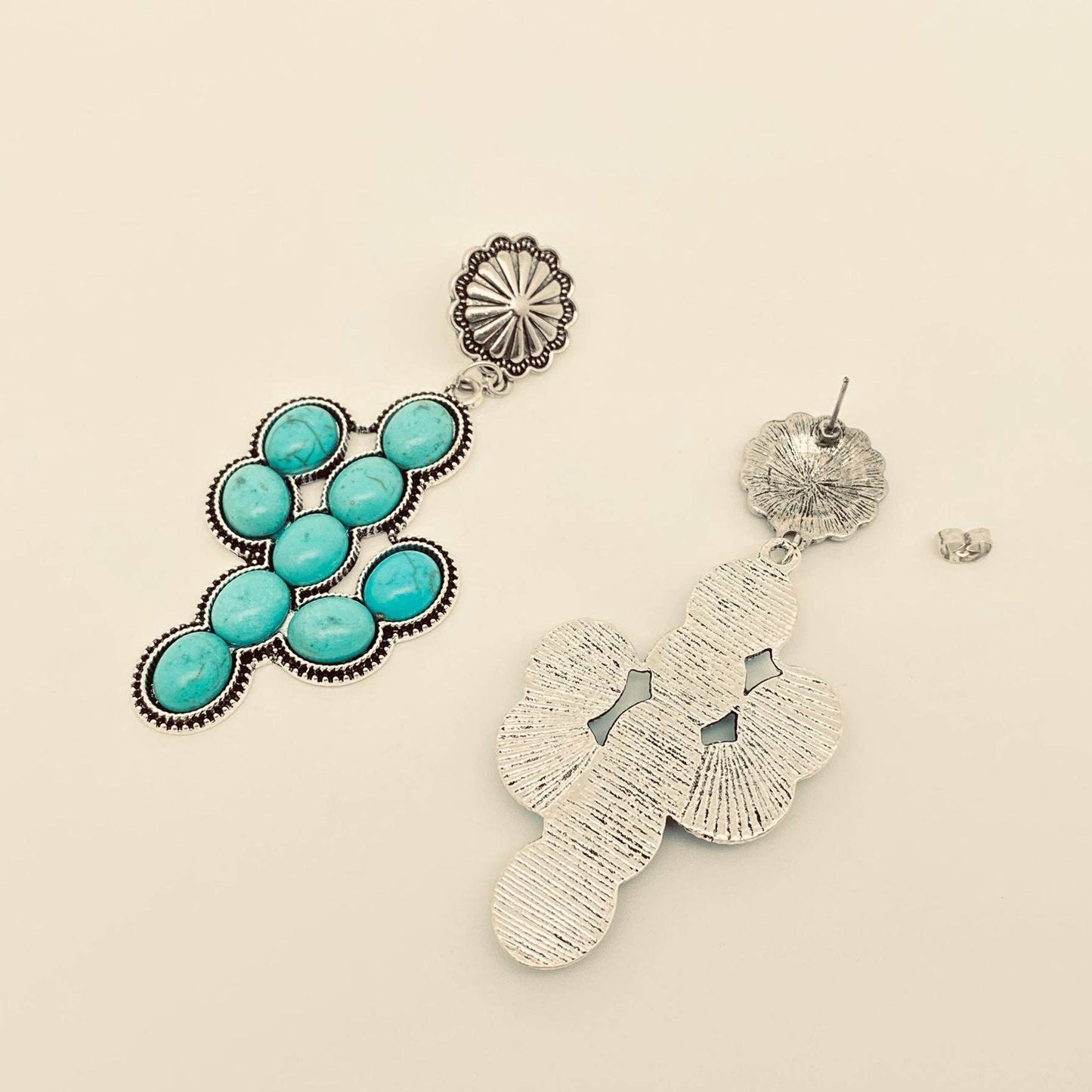 Pair of earrings with turquoise stones and silver designs on a beige background