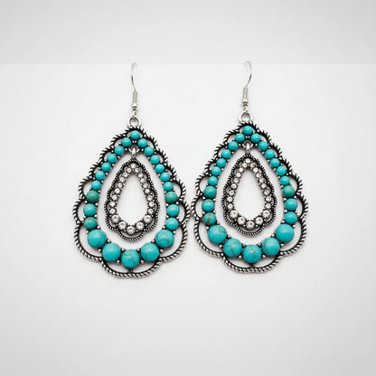 Turquoise beaded earrings on a hand with a plain background